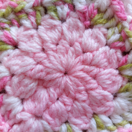 a close up of a pink crochet flower with outer petals in green
