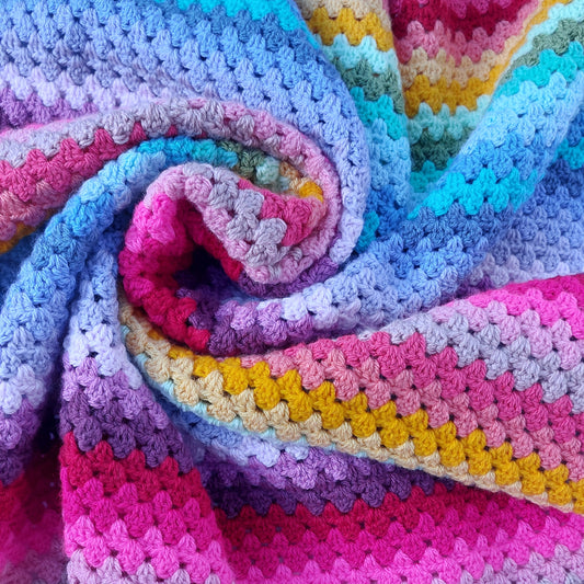 Colorful crocheted blanket with a gradient of pink, purple, blue, and yellow.