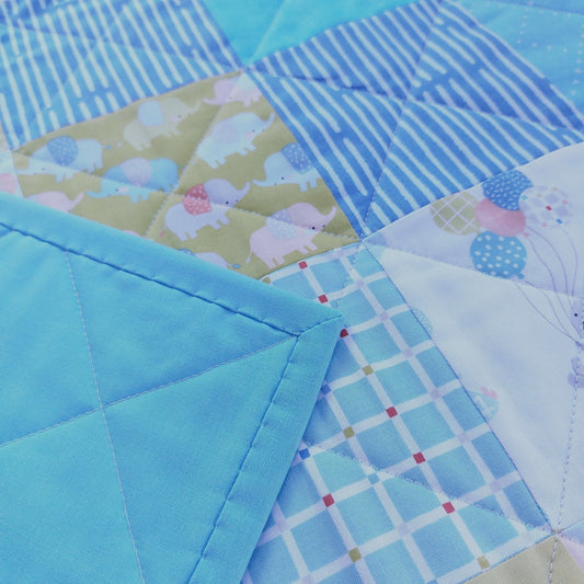 Close-up of a patchwork quilted fabric with multiple blue-toned patterns, including stripes, plaid, elephant print, and solid sections.