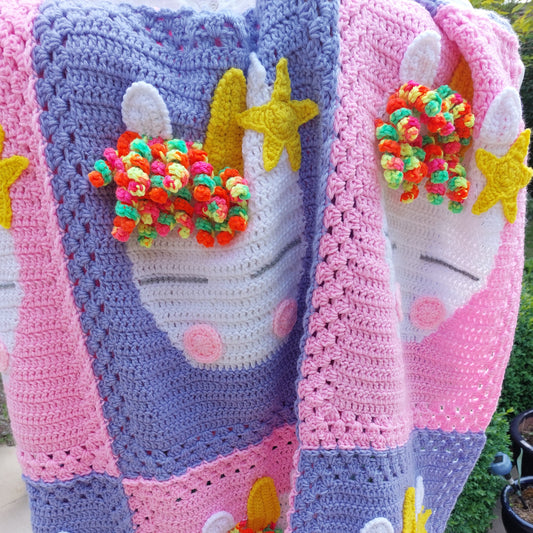 a handmade crochet unicorn blanket made up of pink sections and purple sections with a unicorn head on each one.