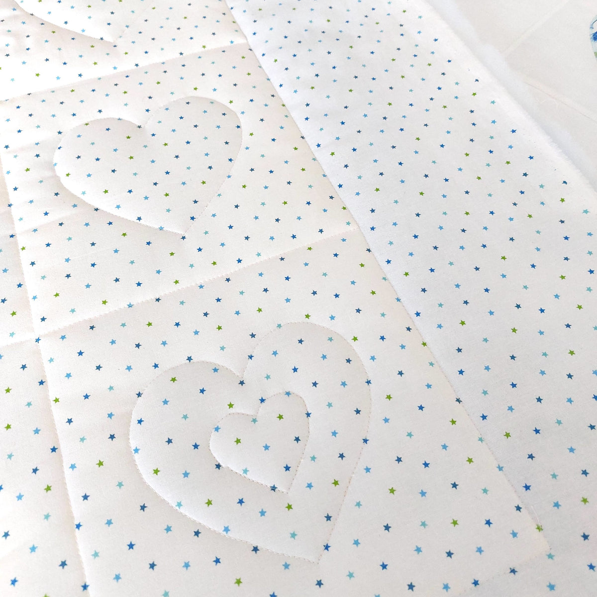 the back of the quilt of white fabric with small blue and green stars all over with the outline of quilted hearts