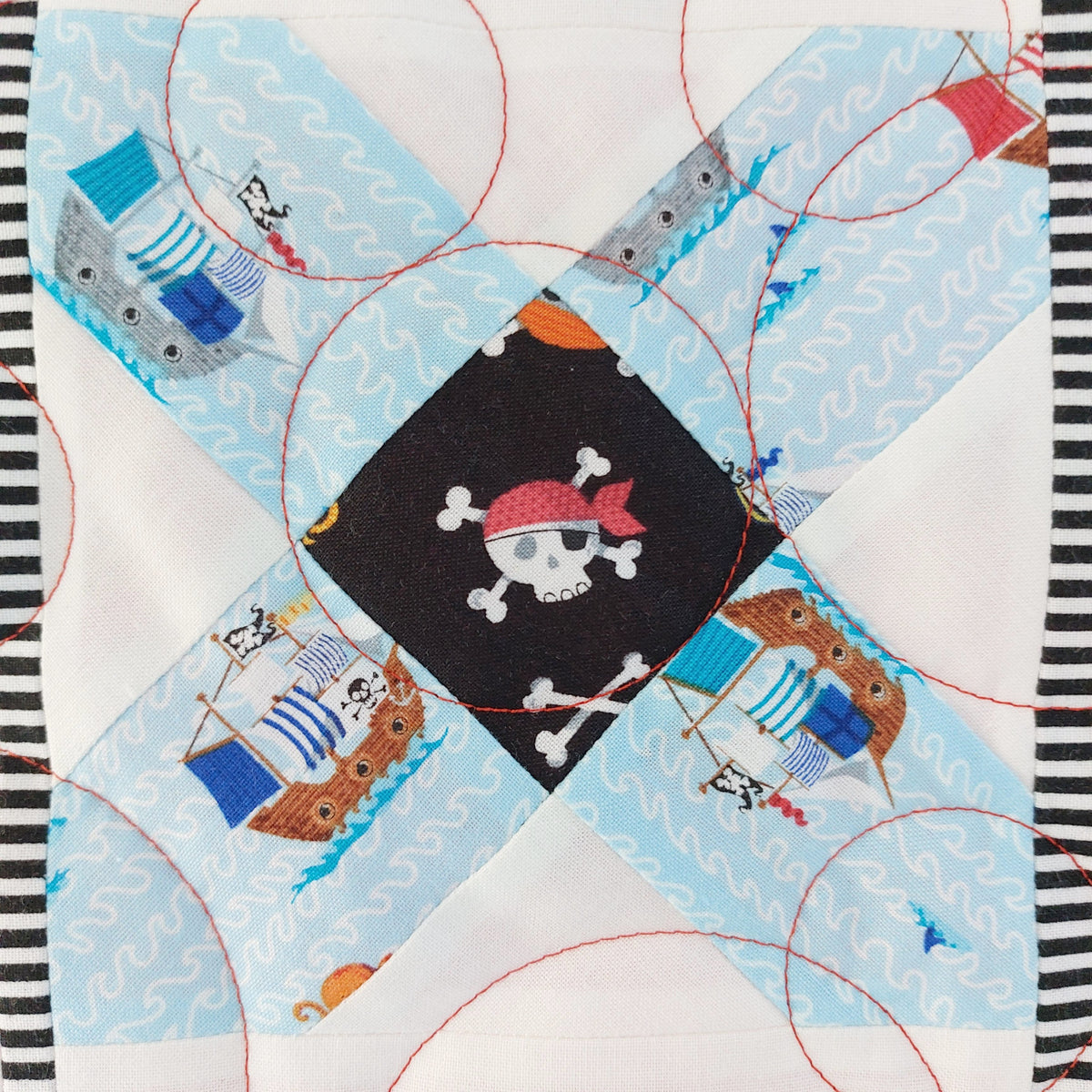 Quilt block with pirate design featuring a skull and crossbones on a blue background.