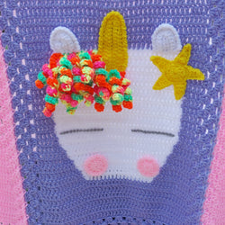 a handmade crochet unicorn blanket white unicorn head with white ears, yellow horn and star and a mane of brightly coloured yarn swirls