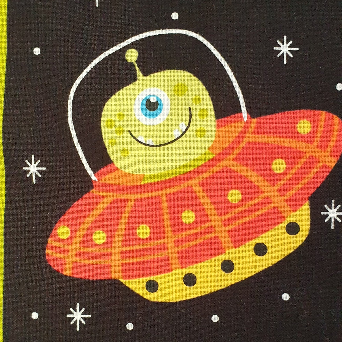 a black cotton background with a green smiling alien sitting in his orange spaceship