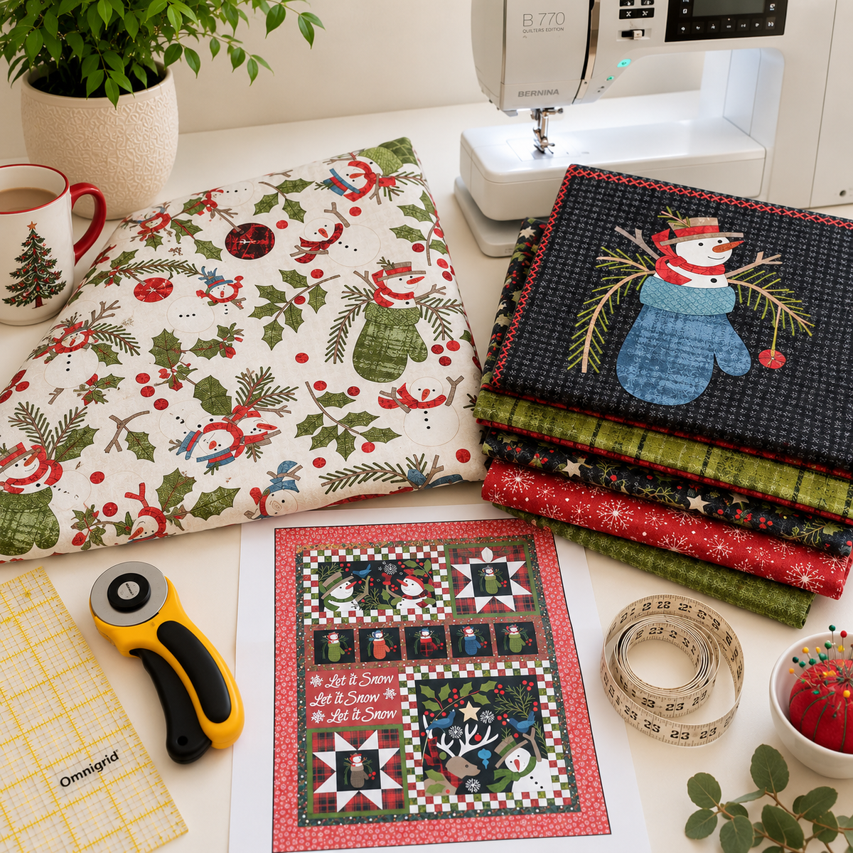 A styled sewing and quilting workspace with a folded quilt featuring a Christmas snowman and holly pattern, a stack of patterned quilts, a sewing machine, a rotary cutter, measuring tape, fabric yardage, and a printed quilt design on a white tabletop.