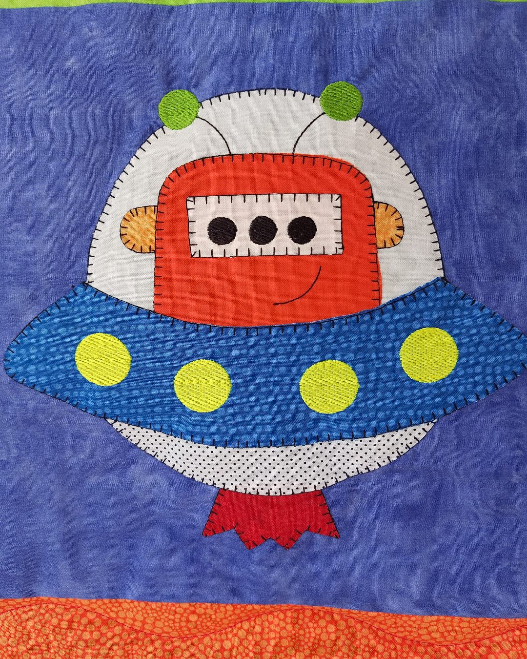an outer space quilt with a large alien spacecraft on a blue fabric background