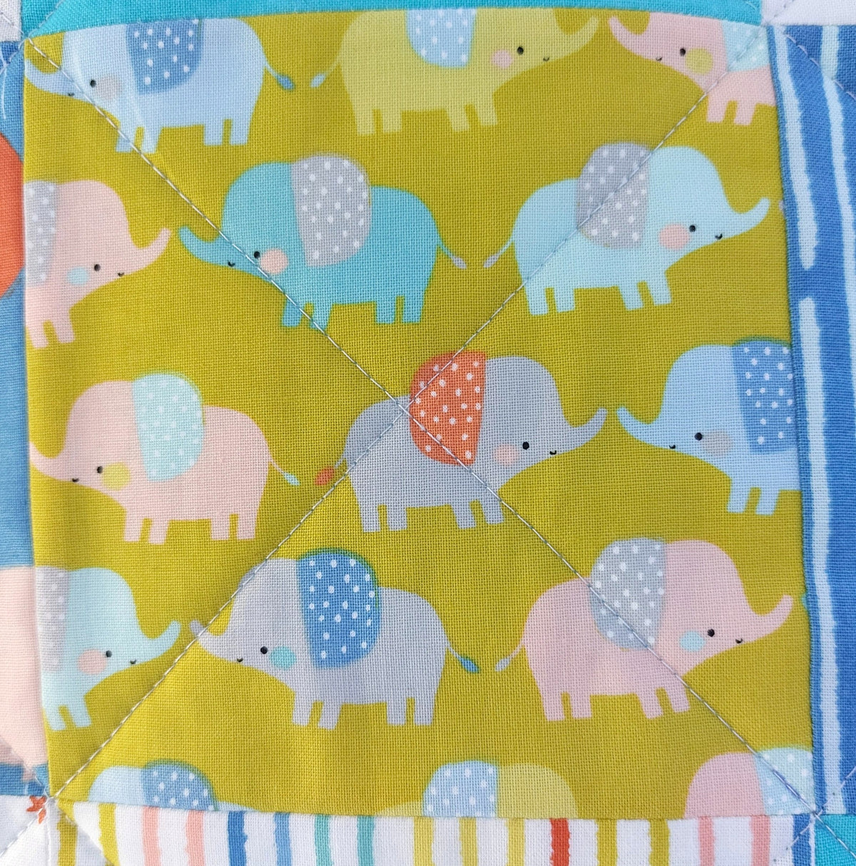 A close-up of a quilted fabric square featuring a playful pattern of pastel elephants in blue, pink, and gray on a bright yellow-green background, finished with striped borders.