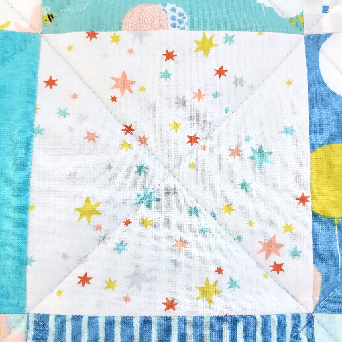 A close-up of a quilted fabric block featuring a white center panel with a scattered print of colorful stars in yellow, orange, red, and light blue, surrounded by coordinating patterned borders.