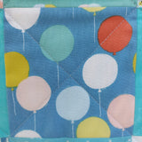 Delivered with love patchwork baby quilt, Fabric square with colourful balloon pattern on a blue background