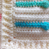 a corner of the handmade crochet rainbow bobble blanket showing the cream border