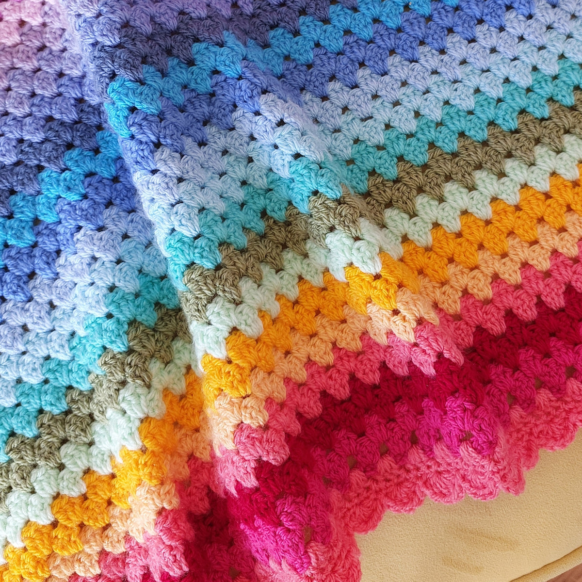 Colorful crocheted blanket with a gradient of blue, green, orange, pink, and purple.