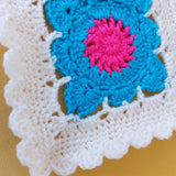 Crocheted square with blue and pink flower design on a white border.