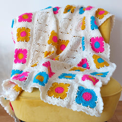 bright yellow, blue. pink and white crochet flowers make a blanket draped on a yellow chair