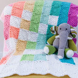 handmade rainbow baby blanket on a chair with a stuffed grey elephant