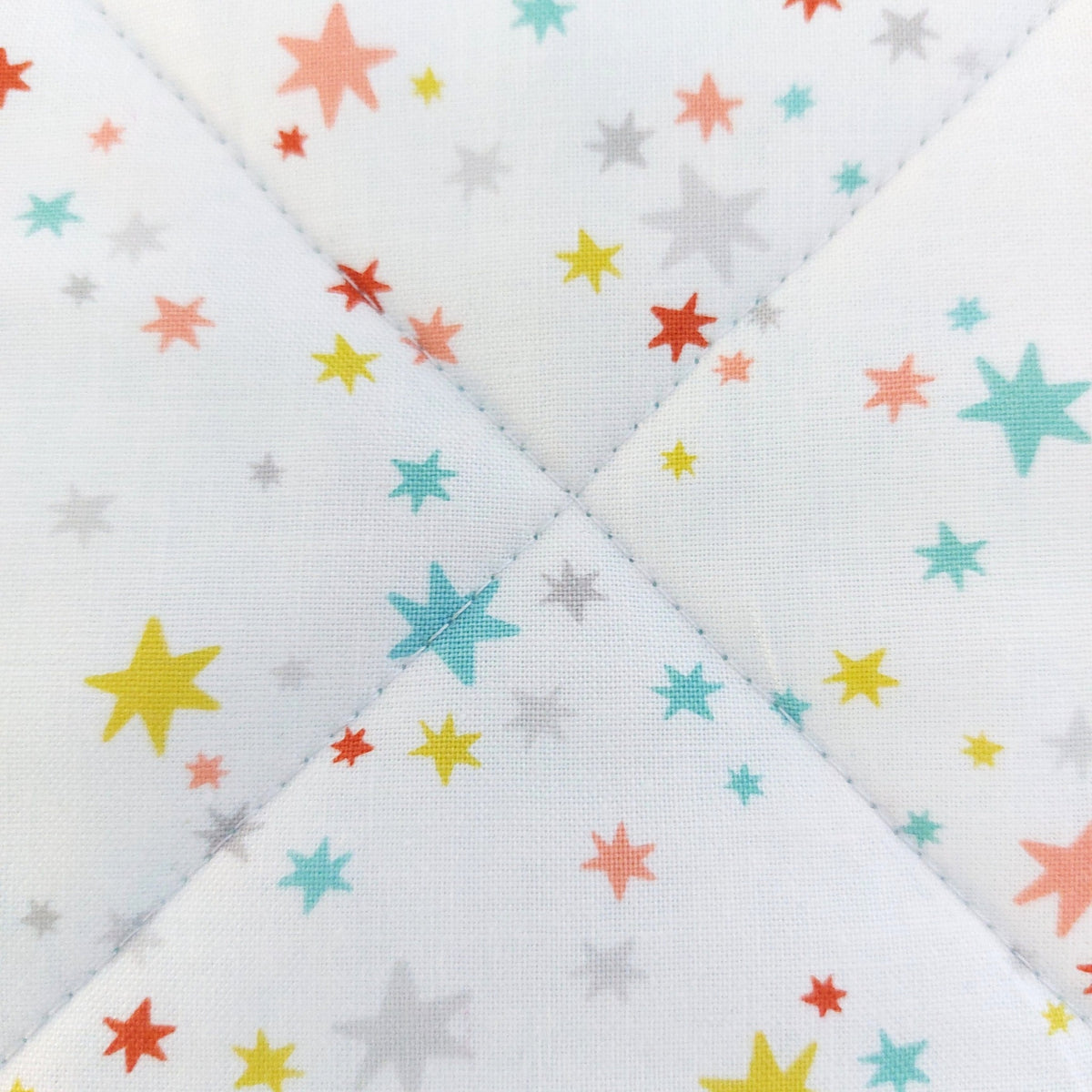 Close-up of a quilted fabric featuring a white background with a scattered pattern of stars in pastel yellow, orange, red, and light blue.
