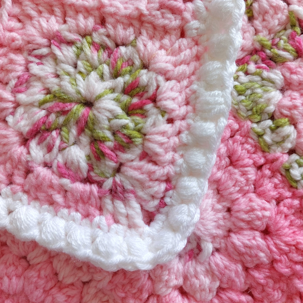 a corner of the pink and green flower square blanket showing a white bobble border