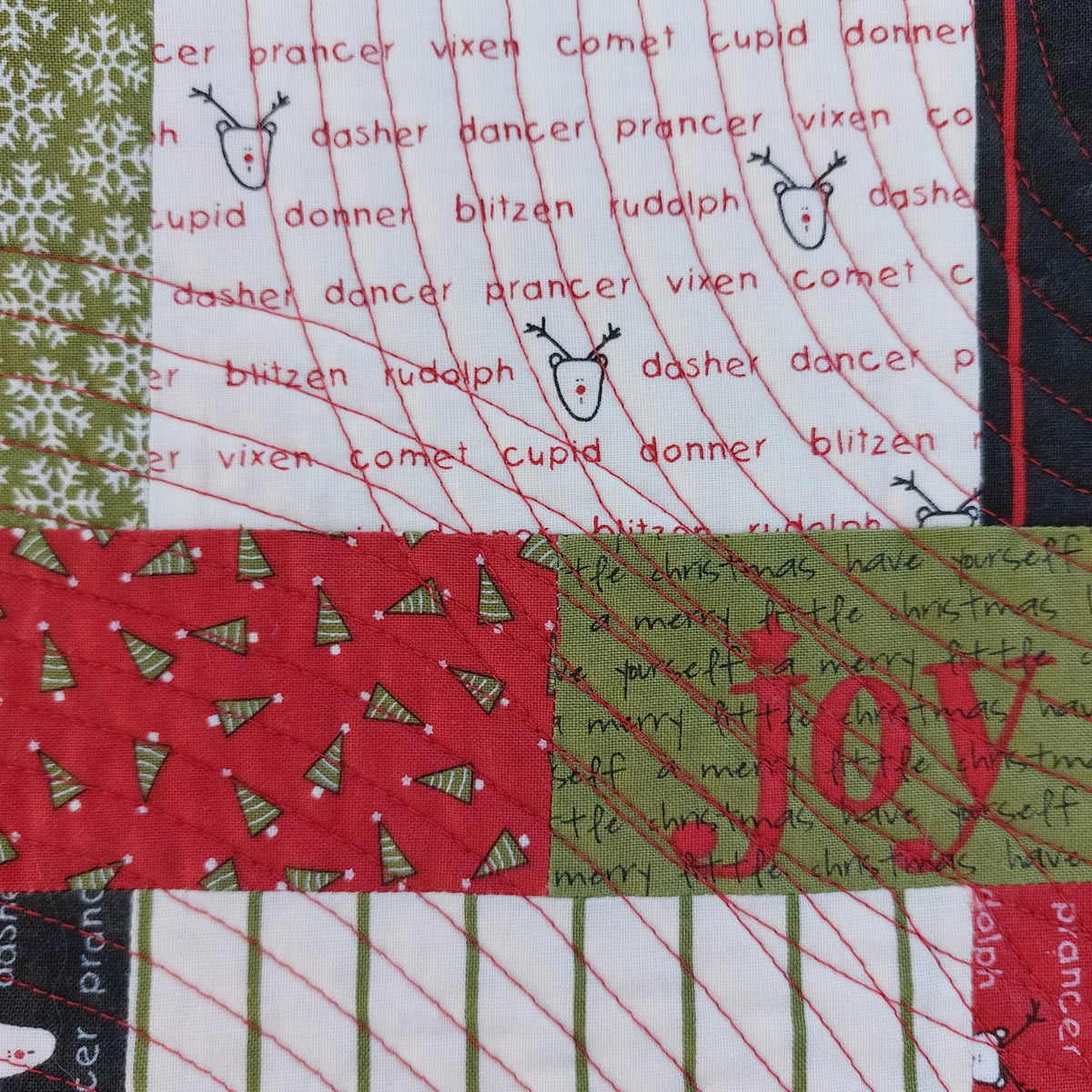Close-up of a Christmas patchwork quilt showing the names of all the reindeer and the red circular quilting.