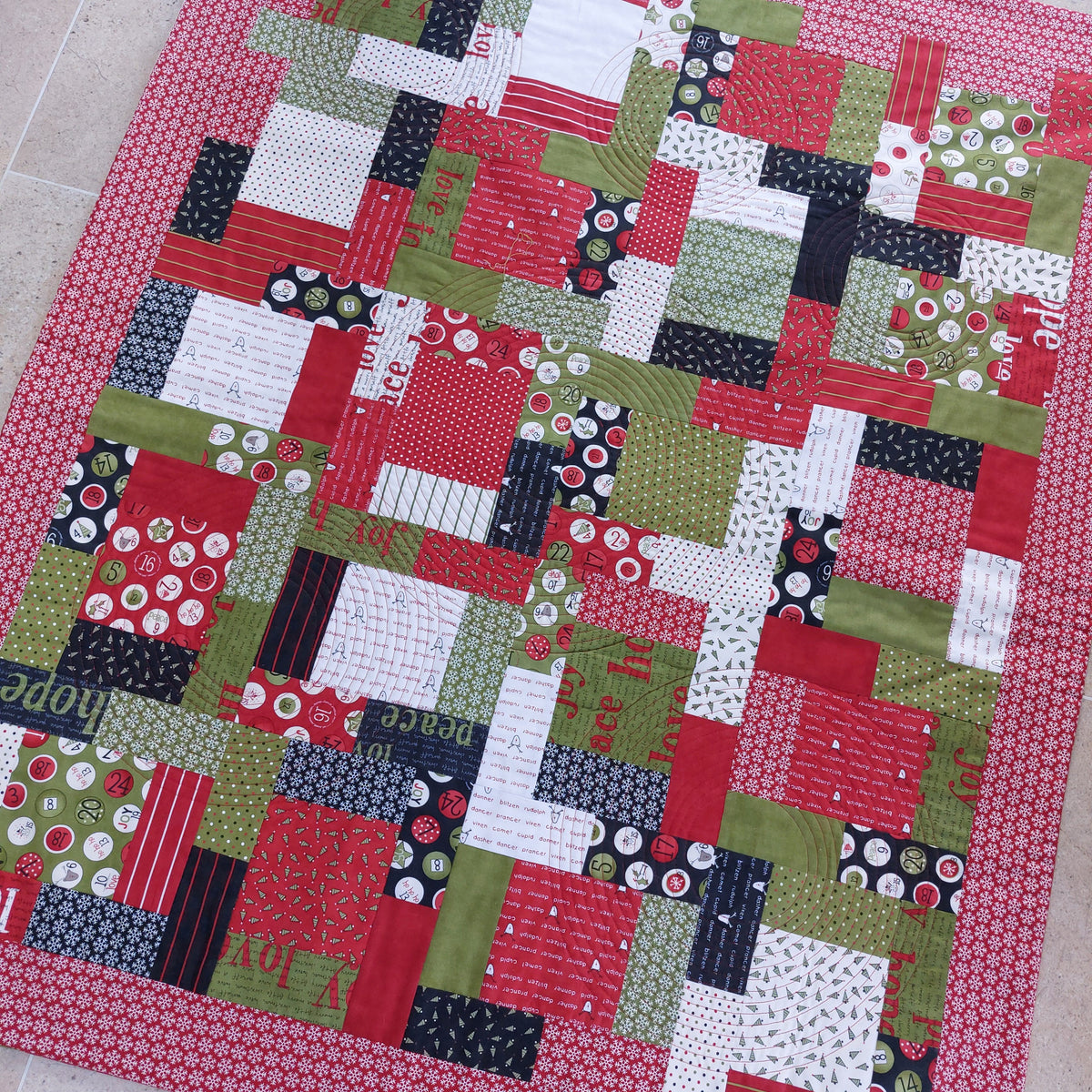 Patchwork quilt with a variety of colourful fabric squares on a tiled floor.