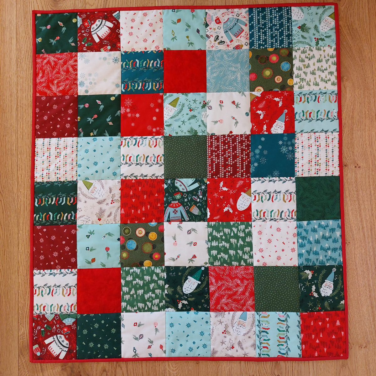 an overhead view of a patchwork baby quilt that features Christmas fabric of trees, sweaters, socks and Santas