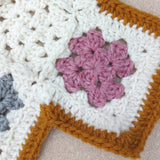 close up of the handmade crochet baby blanket showing a pink and cream square with the gold border