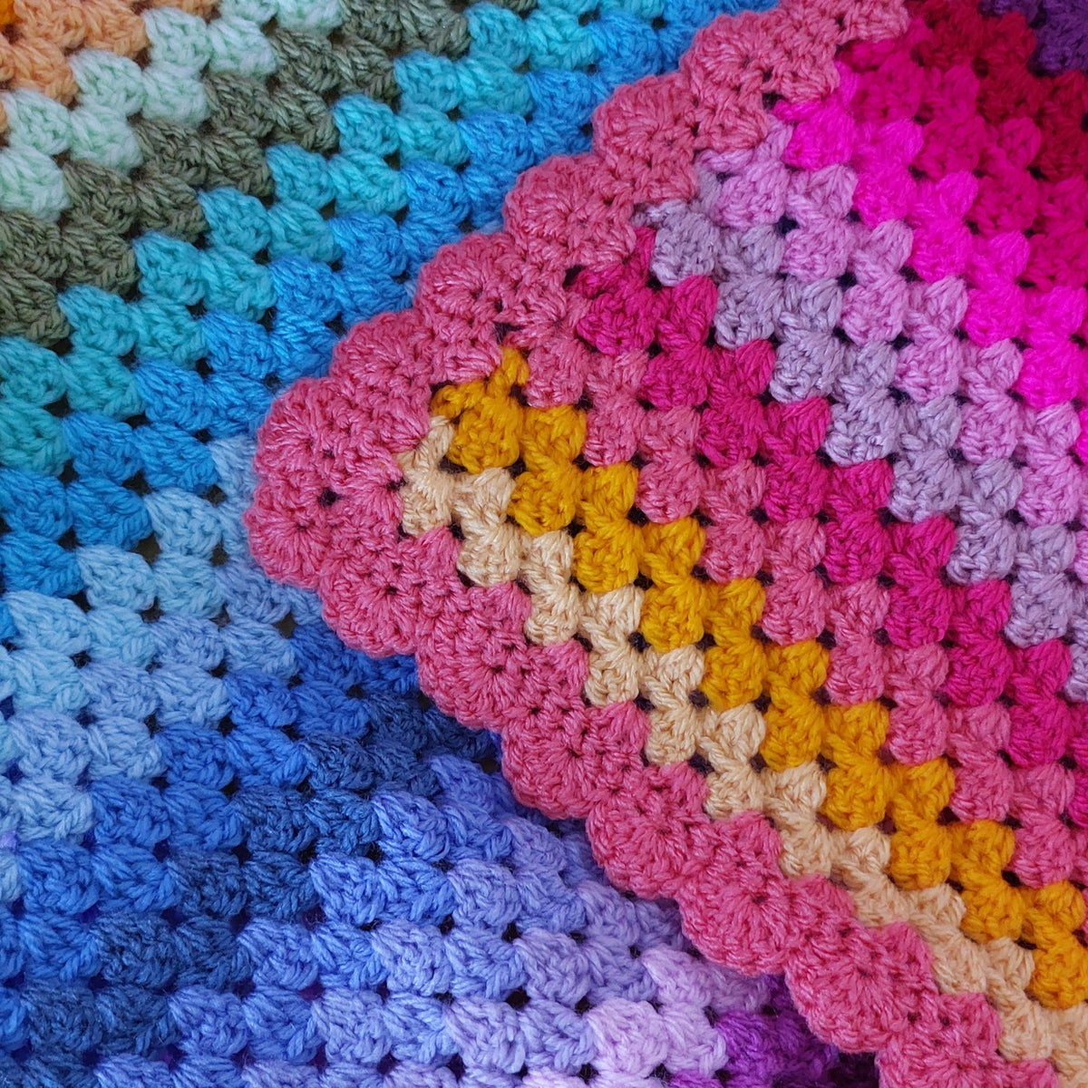 Close-up of a colorful crocheted blanket with pink, blue, and yellow patterns.