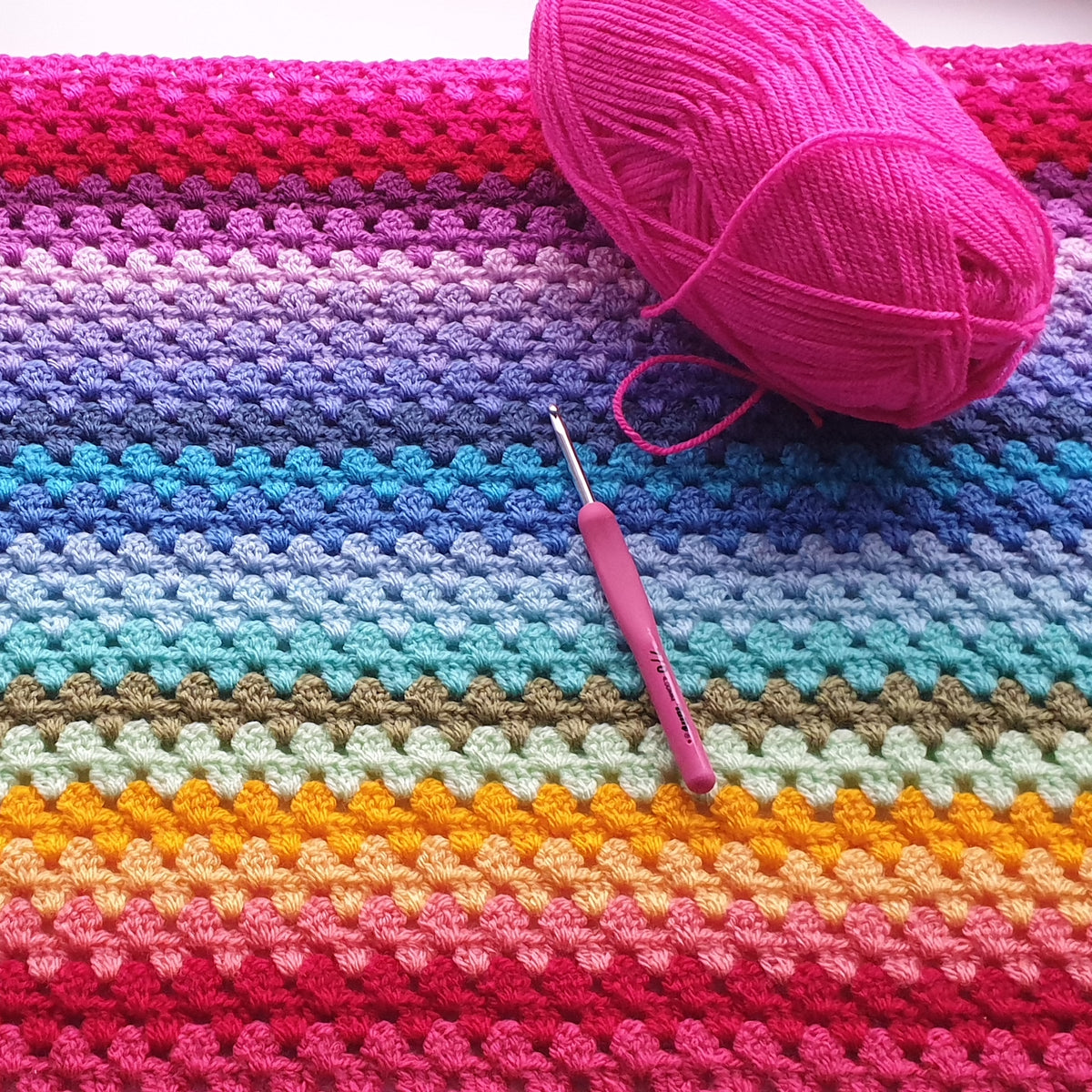 Colorful crocheted blanket with a pink yarn ball and crochet hook on top