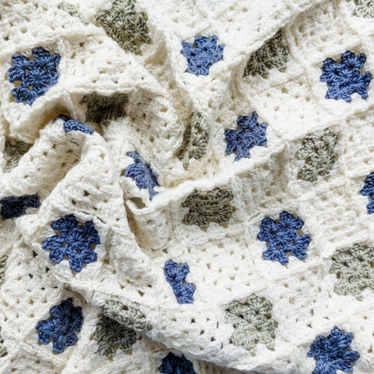 the crochet granny squares baby blanket in blue, cream, and green scrunched up 