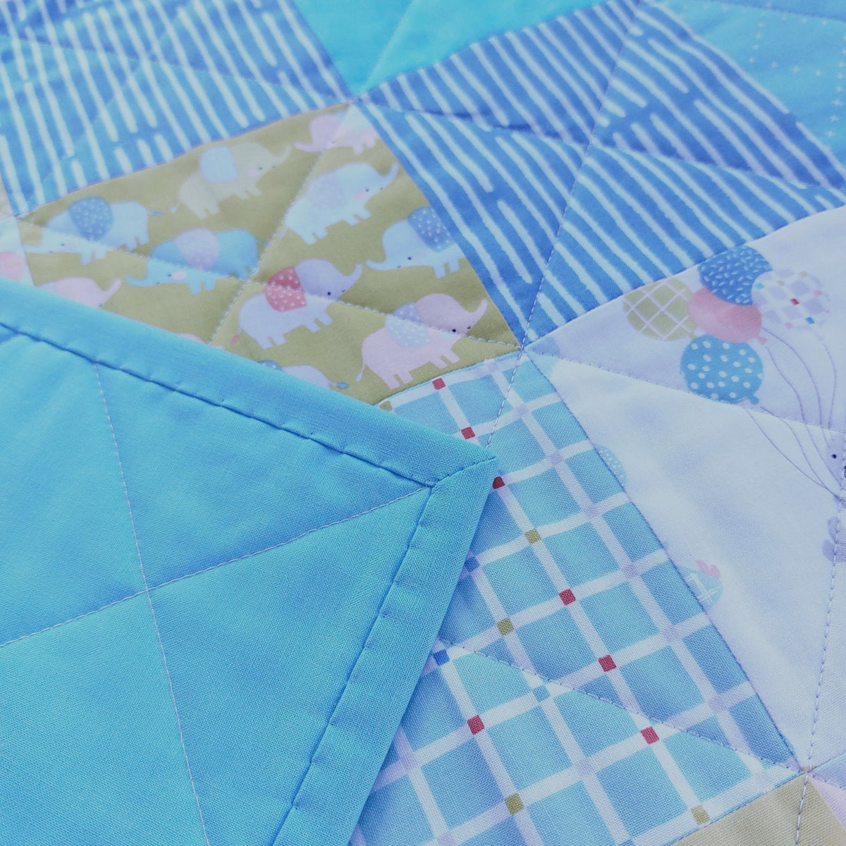 Close-up of a patchwork quilted fabric with multiple blue-toned patterns, including stripes, plaid, elephant print, and solid sections.