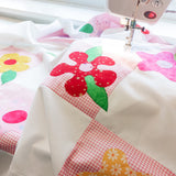 the pink check and white patchwork quilt under the foot of a sewing machine