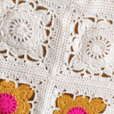 Close-up of a crocheted blanket with floral patterns in white, yellow, and pink.