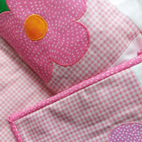 A pink checked quilt folded to show a big pink flower with an orange centre with a matching binding to the quilt.