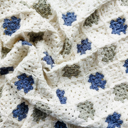 the crochet granny squares baby blanket in blue, cream, and green scrunched up 