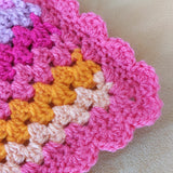 Close-up of a crocheted fabric with pink, orange, and beige colors on a beige background.
