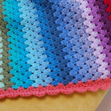 Multicolored crocheted blanket with a gradient of blue, purple, pink, and green.