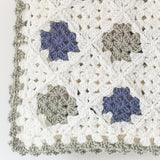 close up of a baby blanket showing green, blue and cream squares with a green frill edging