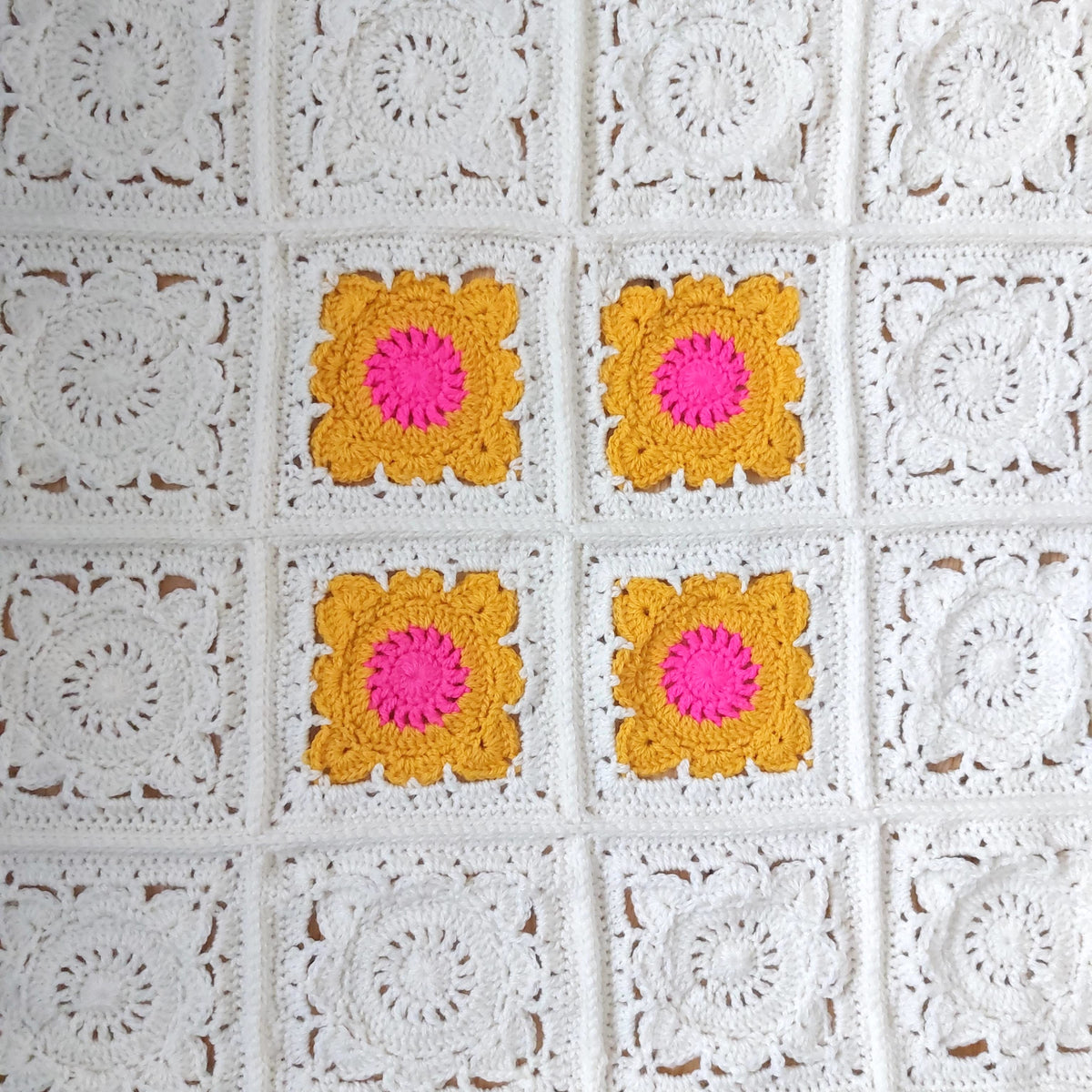 16 granny squares 12 of which are white and the others are bright pink and gold