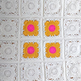 16 granny squares 12 of which are white and the others are bright pink and gold