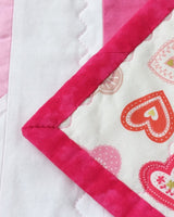 the front of the quilt showing a pink heart with the back of the quilt folded over the front showing hearts on the back