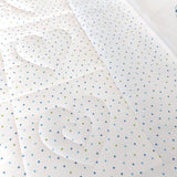 the back of the quilt of white fabric with small blue and green stars all over with the outline of quilted hearts
