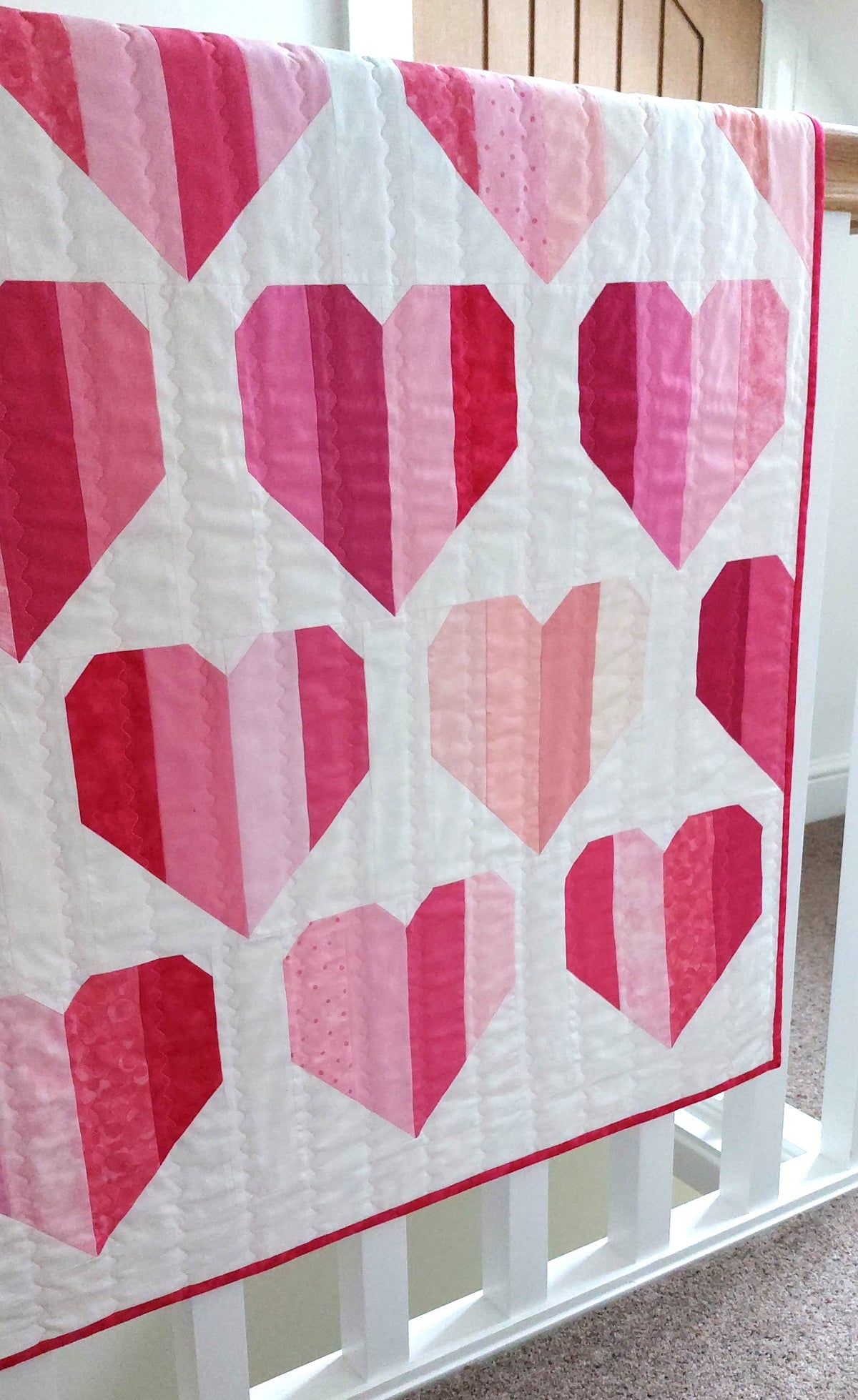 a quilt of with a white background a different coloured pink hearts folded over a banister