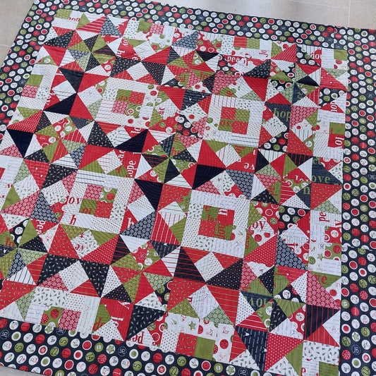 Colourful quilt with a geometric pattern of Christmas fabrics on a checkered floor