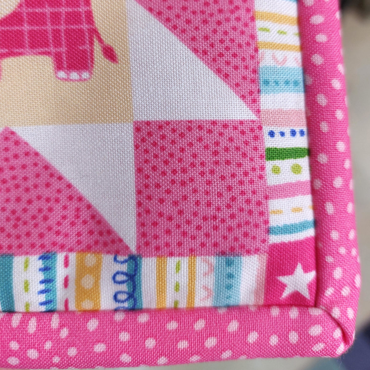 the corner of the quilt is shown with the pink spotted binding 