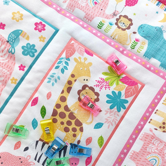 Children's quilt with jungle animal patterns and colourful fabric clips on a white background