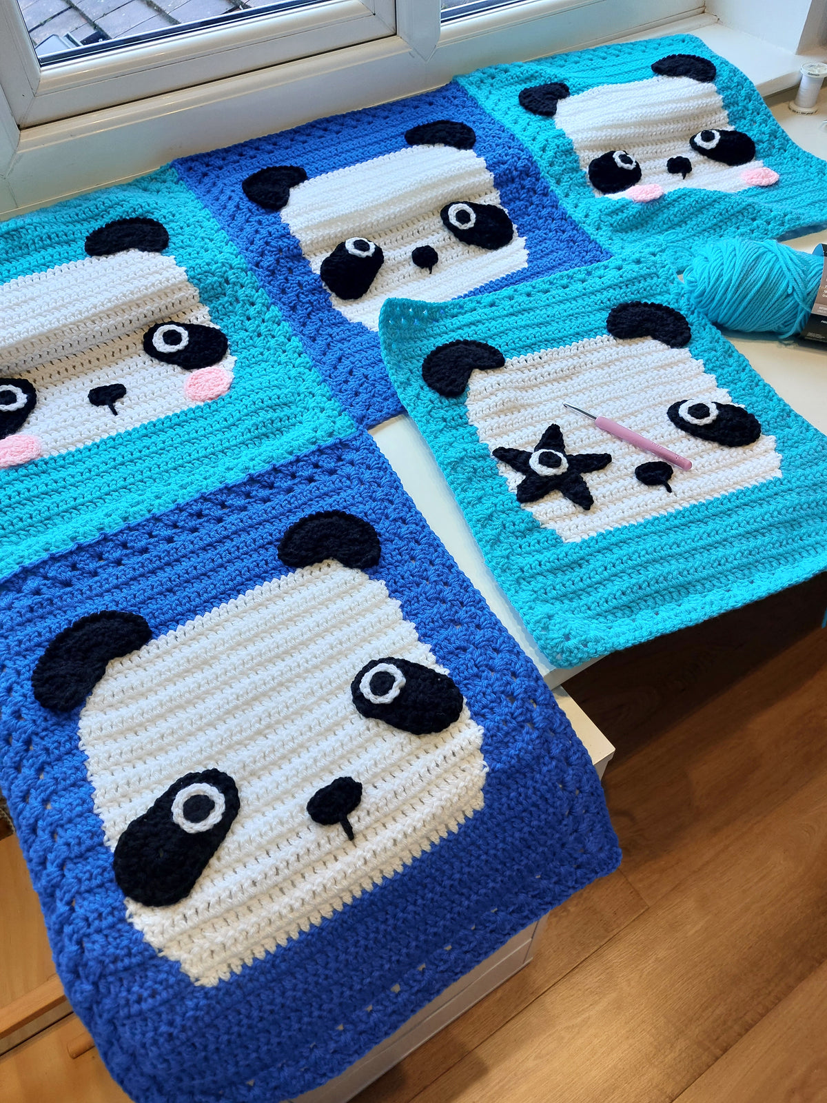 the panda blanket in the making, 5 panda faces on a tables with yarn and a crochet hook
