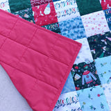 cozy Christmas patchwork baby quilt with depictions of sweaters, mugs, gloves and santa