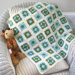 crochet baby blanket with a flower motif in each square. The squares are in blue and green and surrounded by cream.