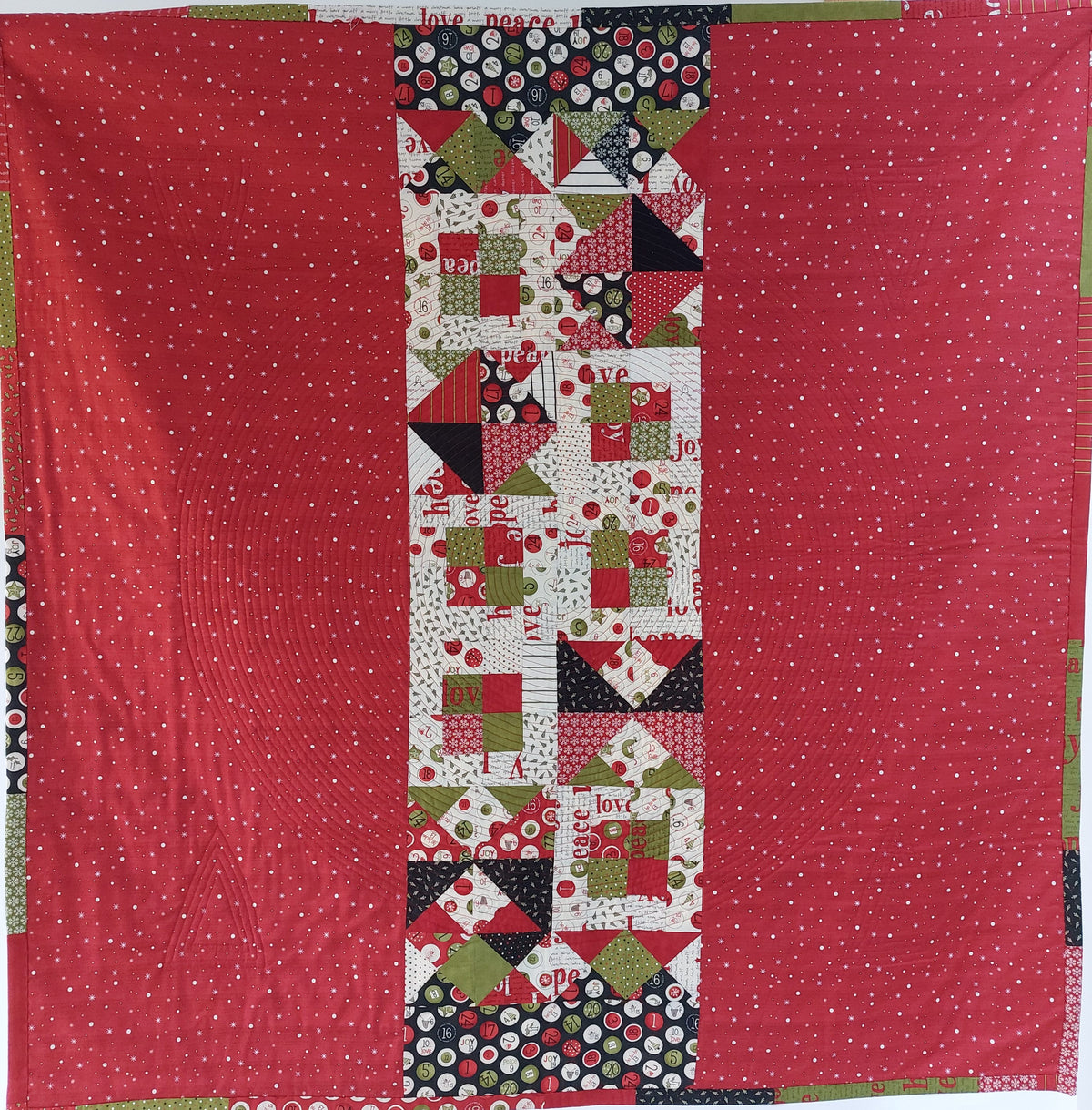 Quilt with a red backing and a central pattern of geometric shapes and text on a white background.