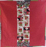 Quilt with a red border and a central pattern of geometric shapes and text on a white background.