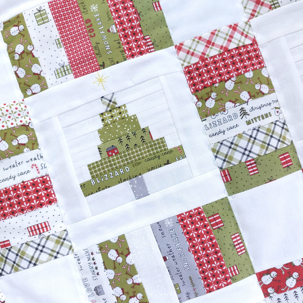 A close-up of a handmade quilted fabric featuring a central Christmas tree patch surrounded by festive red, green, and white patterned blocks.