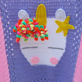 a handmade crochet unicorn blanket white unicorn head with white ears, yellow horn and star and a mane of brightly coloured yarn swirls